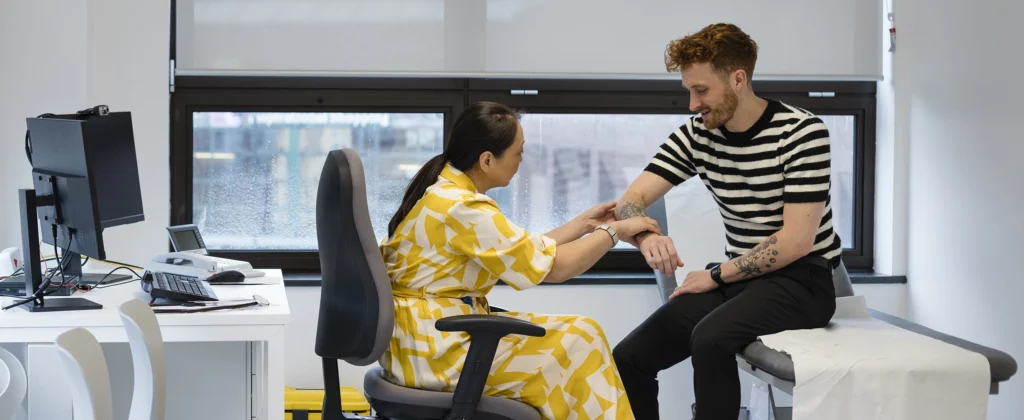 A doctor examines a patient's arm in a clean, bright, modern GP practice.
